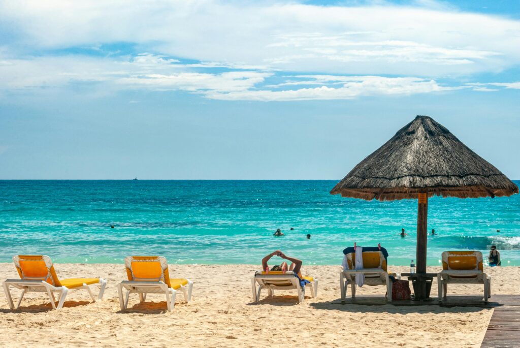 Sunny beach scene in Quintana Roo, Mexico with lounge chairs and thatched umbrella, perfect for relaxation.